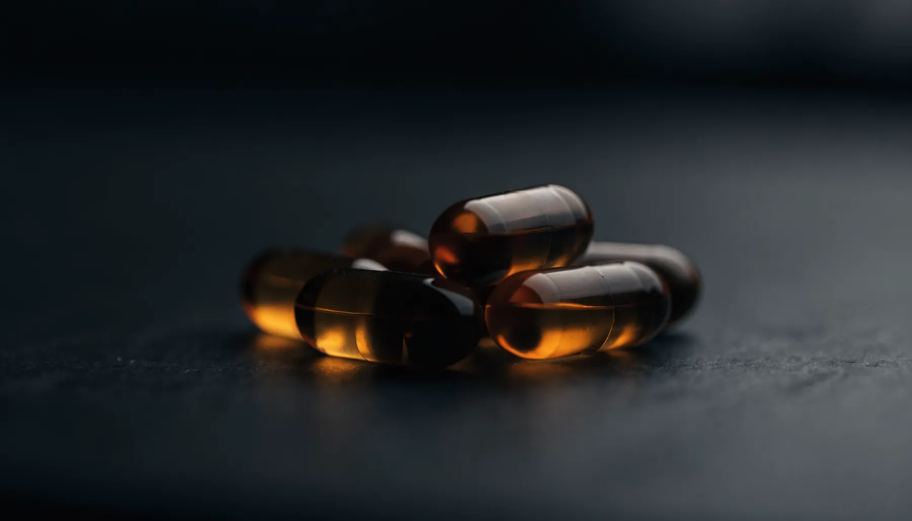 Amber omega-3 softgel capsules lit from the side on a dark surface