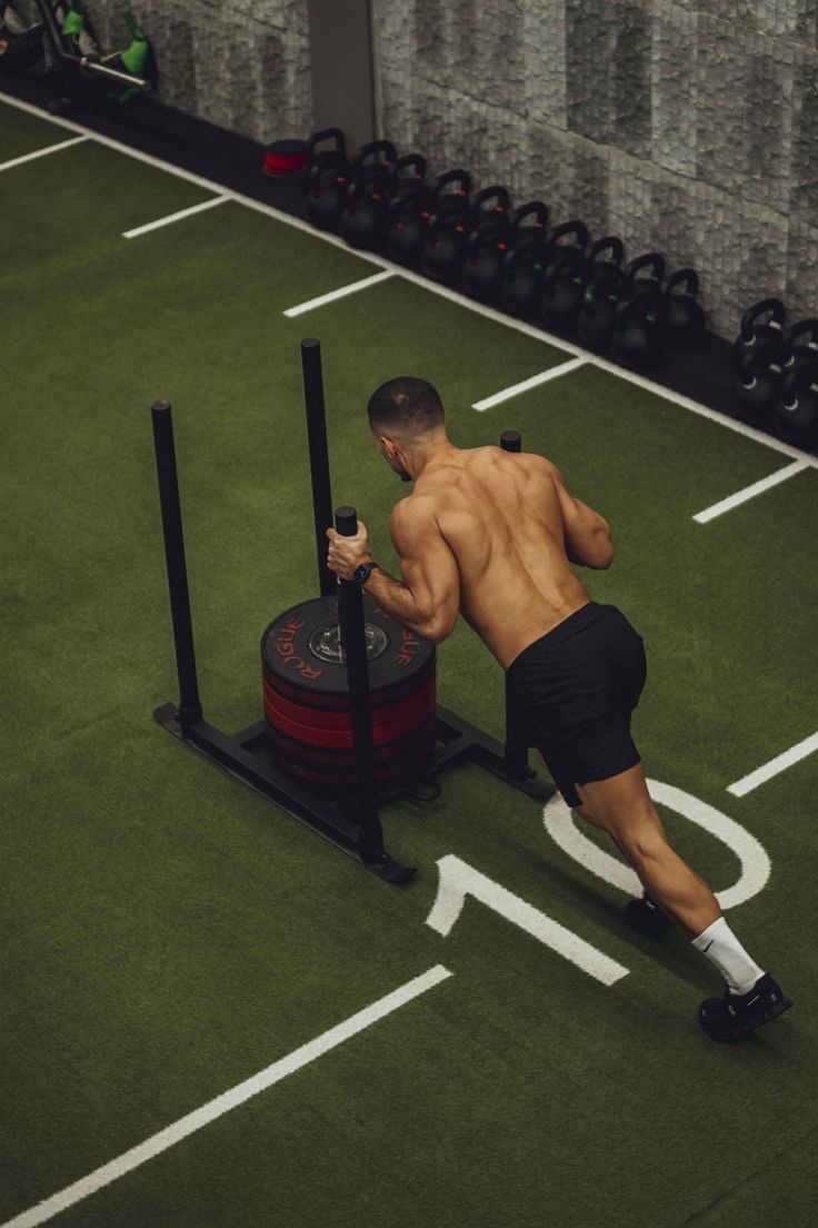 A man pushing a weighted sled across a turf track